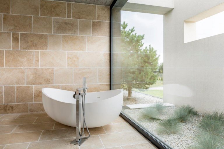 A beautiful modern pedistal bathtub in a spotless Calgary bathroom in front of a very large freshly cleaned window pane